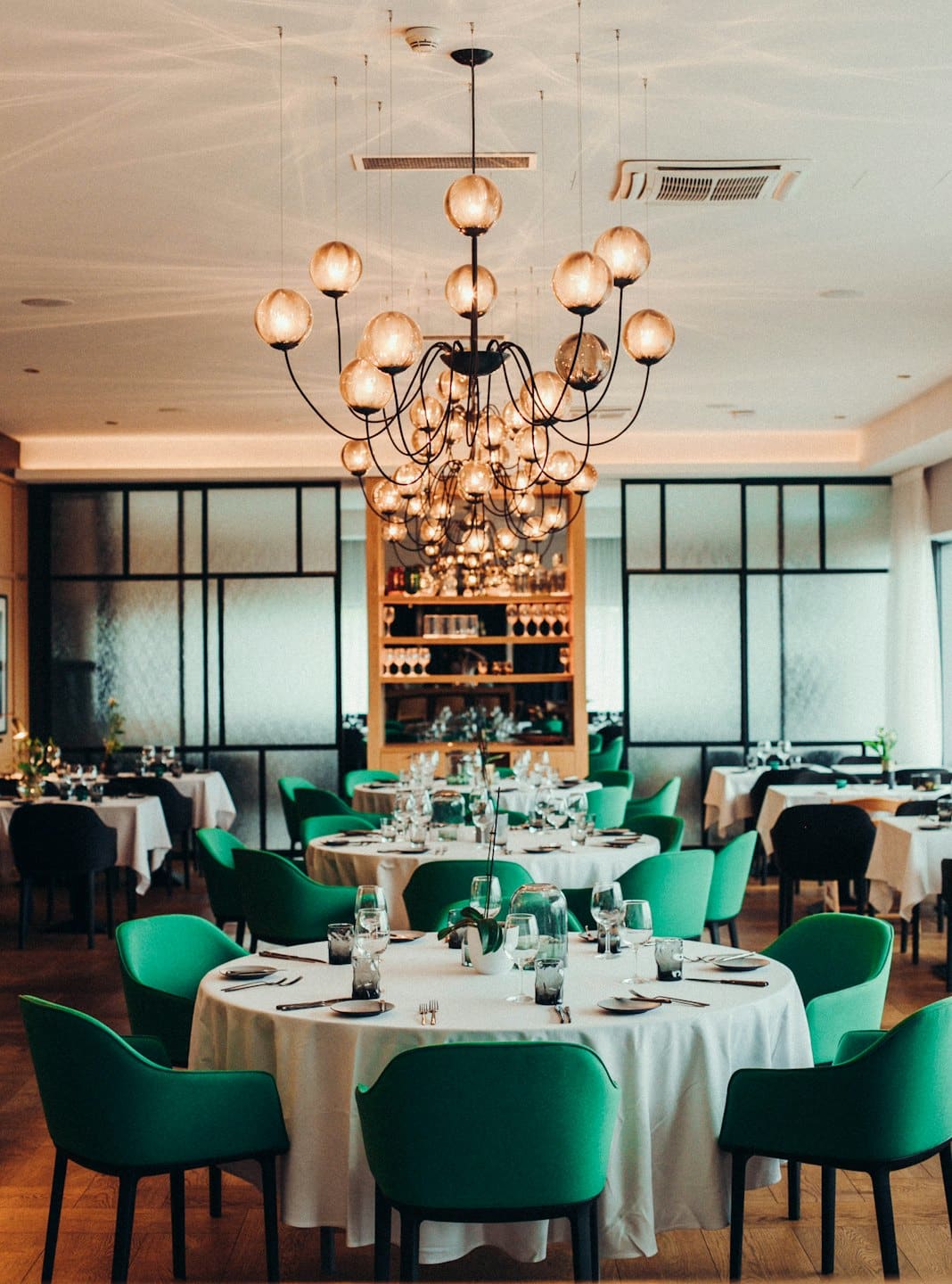 Sala da pranzo elegante di un ristorante con tavoli rotondi e sedie verdi.
