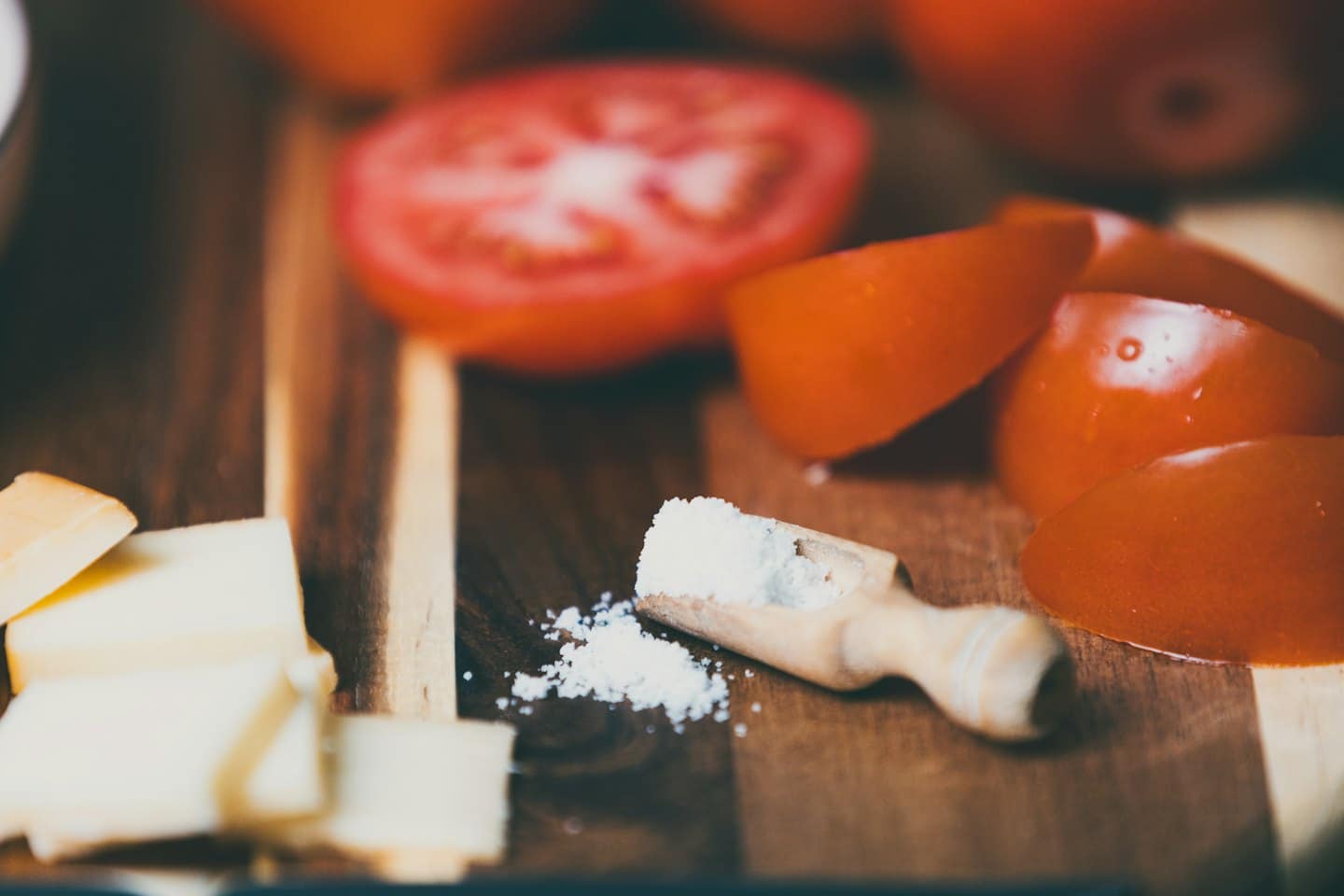 Fette di pomodoro e cubetti di formaggio su un tagliere di legno.