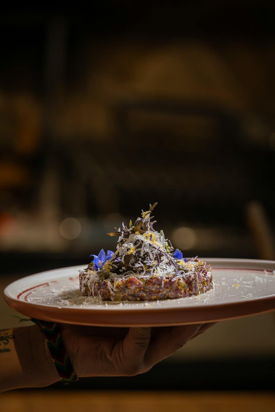 Tartare gourmet con microgreens su piatto bianco tenuto da una mano.