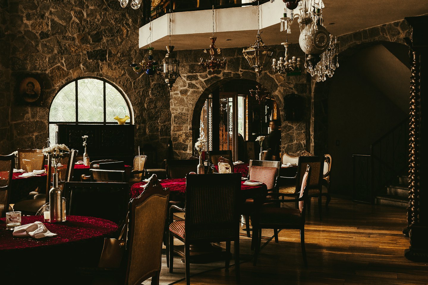 Ristorante rustico vuoto con tovaglie rosse e lampadari ornati.