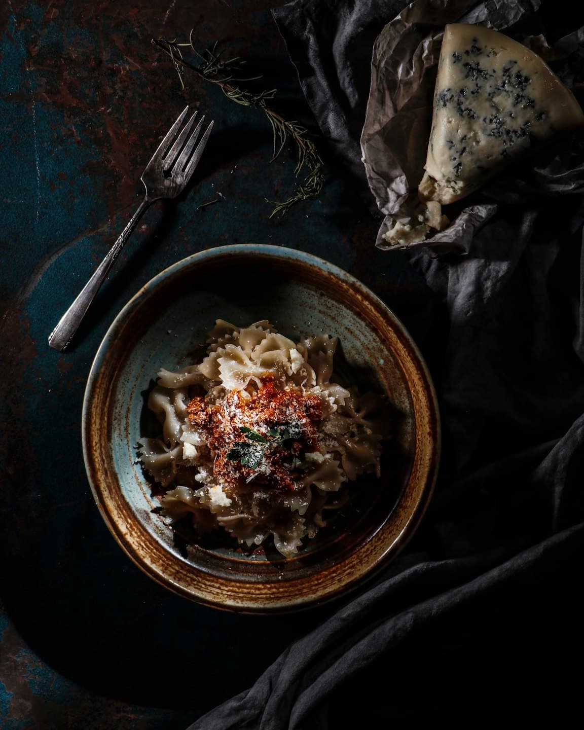 Ciotola di ceramica con pasta farfalle, sugo rosso ed erbe aromatiche.
