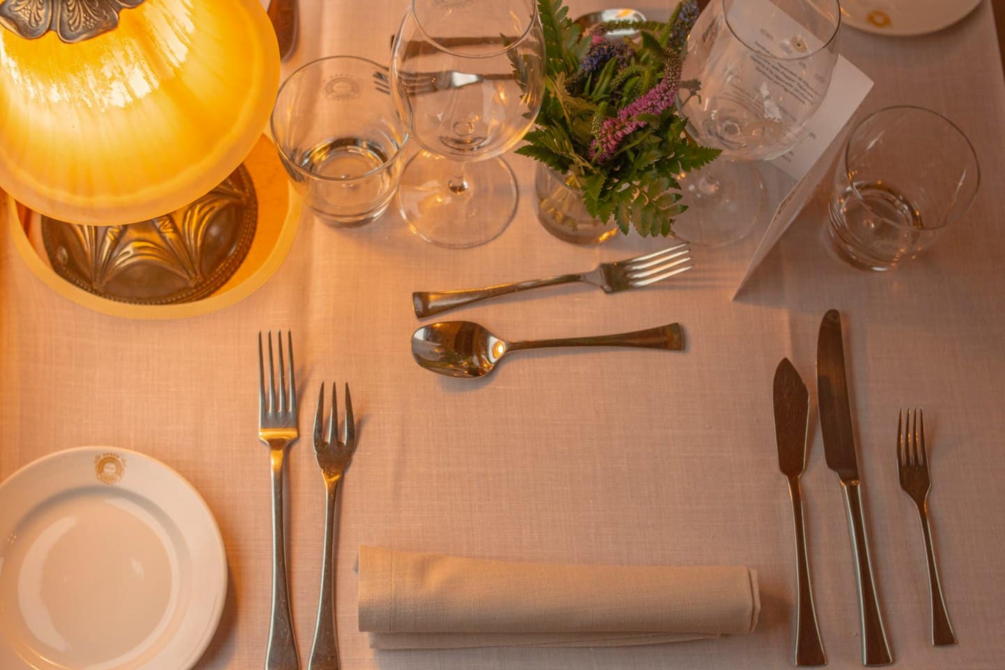 Tavola da pranzo apparecchiata con piatto, posate e centrotavola floreale.