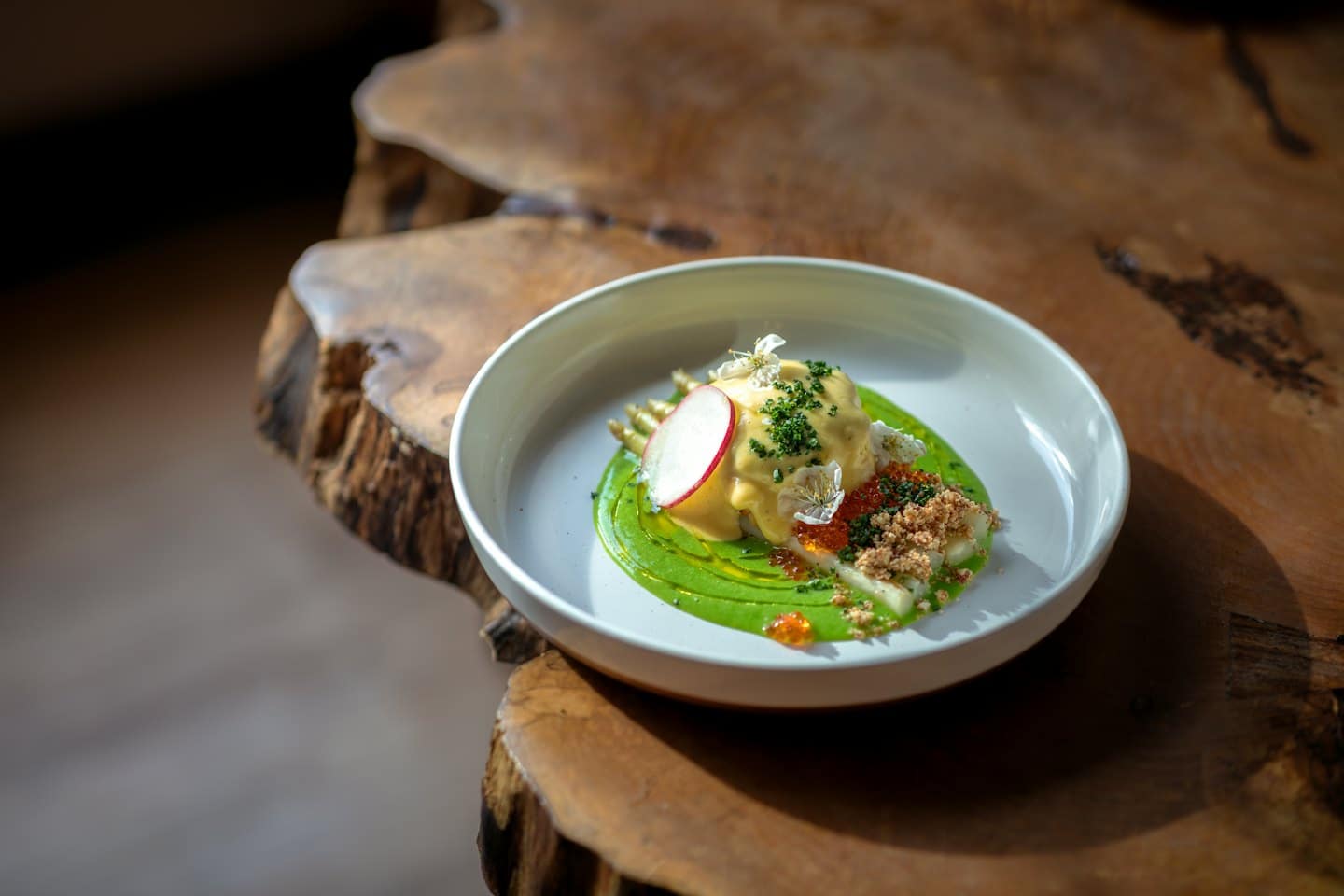 Piatto gourmet con salsa colorata, uova di pesce e fiori su un tavolo di legno.