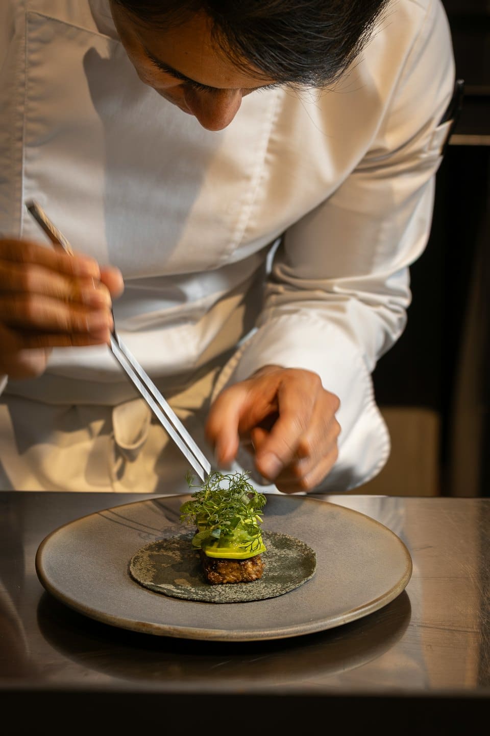 Chef decora attentamente un piatto con microgreens usando una pinzetta.